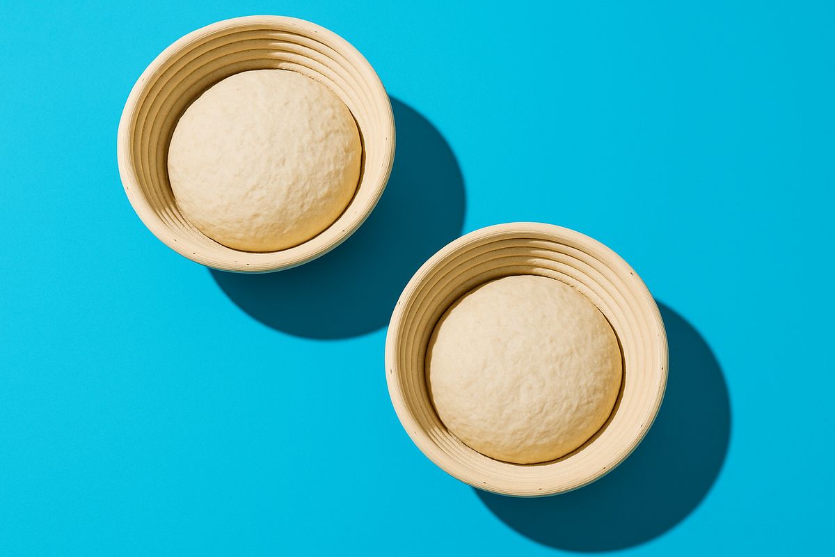 Raw shaped dough resting in proofing baskets, bright